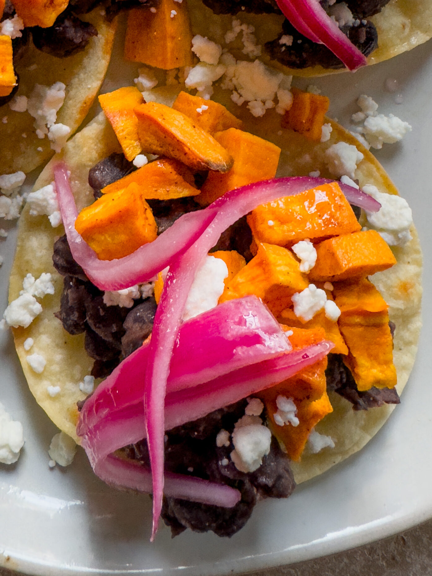Top tostada with pink pickled onions and feta cheese