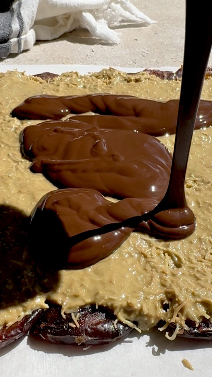Pouring melted chocolate atop creamy kataifi layer of Dubai chocolate date bark. 