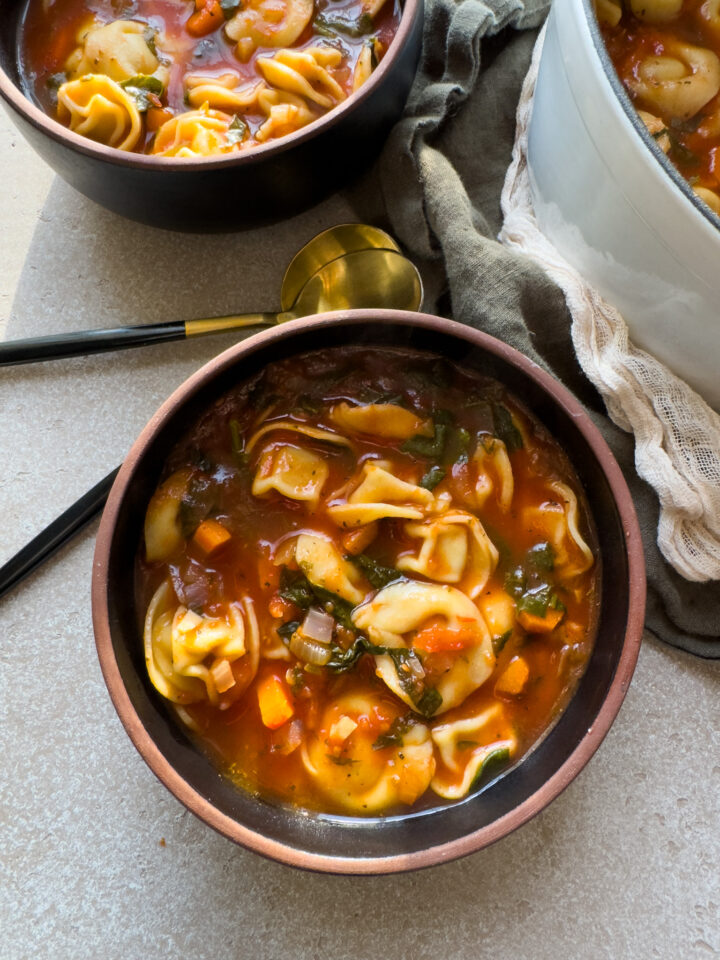 top down view of a bowl of tortellini soup with a black spoon alongside