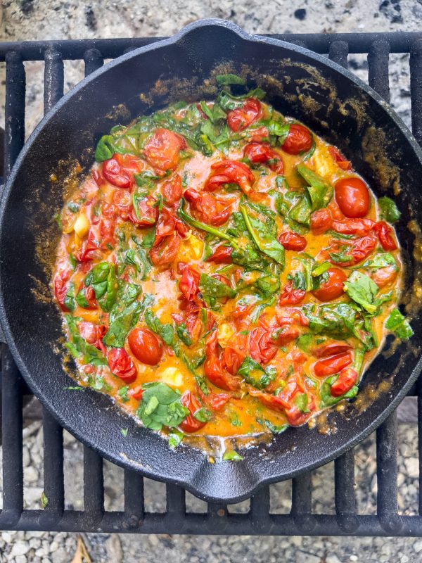 skillet over open fire with tomato sauce and basil stirred together